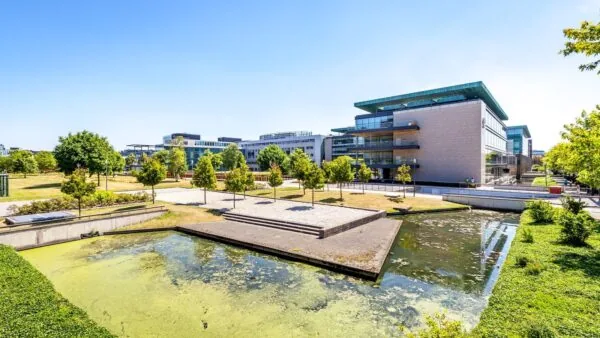 Modern kantoorgebouw aan het water in Kessler Park met groenstroken en bomen op een zonnige dag.